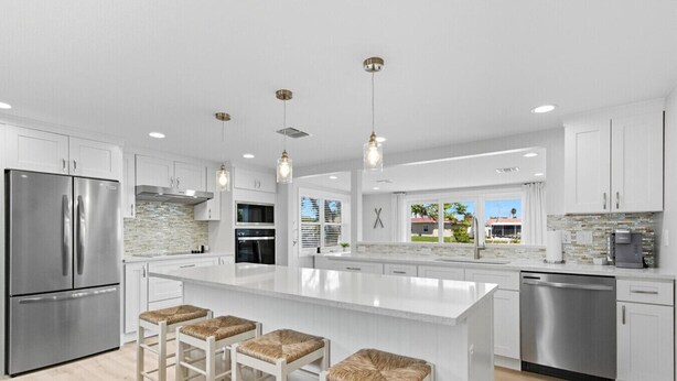 A modern kitchen with white cabinetry, stainless steel appliances, and a large island with bar stools. - Waterfront Retreat W / Floating Dock & Kayaks (New Port Richey)
