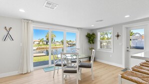 A modern room with a dining table, chairs, and a view of a swimming pool and greenery outside. - Waterfront Retreat W / Floating Dock & Kayaks (New Port Richey)