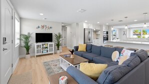 A modern living room with a sofa, coffee table, and TV. There is a kitchen area with cabinets and a refrigerator. - Waterfront Retreat W / Floating Dock & Kayaks (New Port Richey)