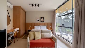 A hotel room with a bed, bedside tables, a chair, a fireplace, and a large window with a view of the outside.