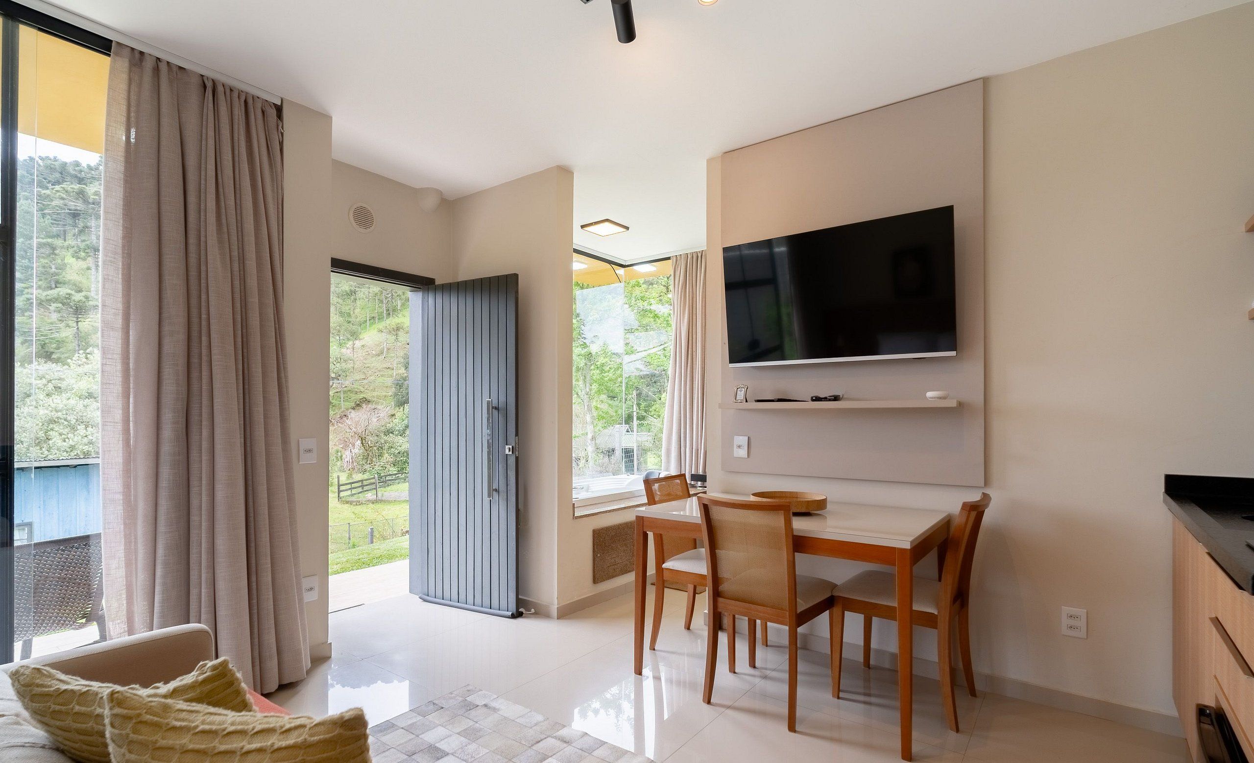 A modern living room with a flat-screen TV, wooden dining table, and chairs.