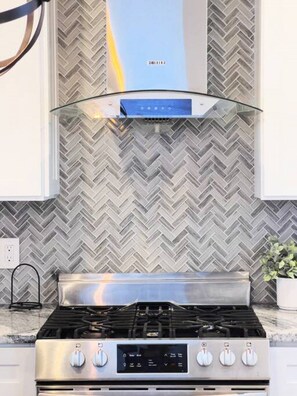A kitchen with a stainless steel stove, a modern range hood, and a herringbone-patterned backsplash. - Ramblei near SJU & CHOP | 8-Bedroom House (Philadelphia)
