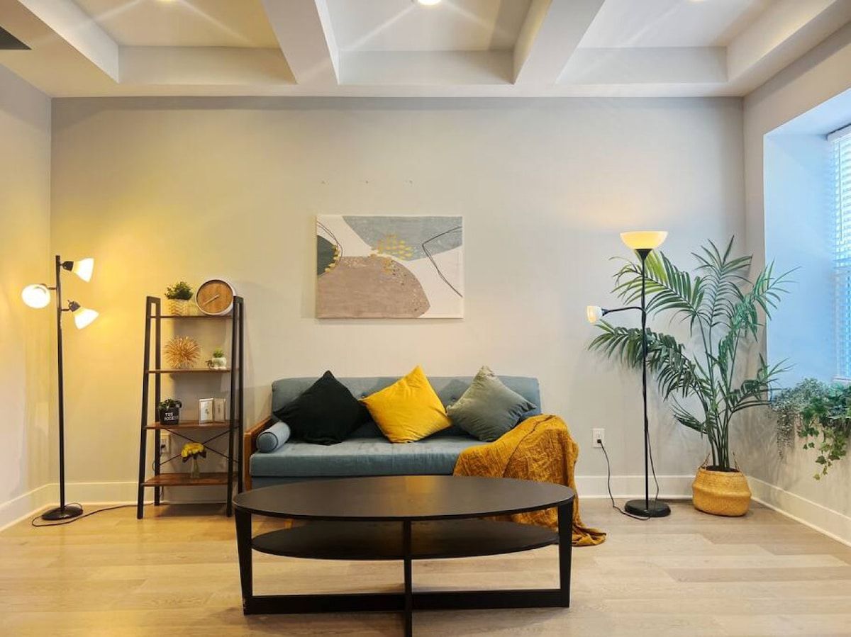 A modern living room with a sofa, a coffee table, a floor lamp, a bookshelf, and a potted plant.