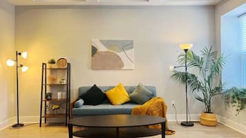 A modern living room with a sofa, a coffee table, a floor lamp, a bookshelf, and a potted plant.