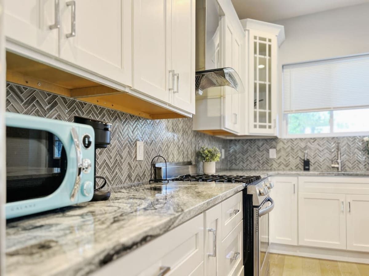 A kitchen with white cabinets, a microwave, a stove, and a herringbone-patterned backsplash.
