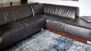 A modern living room with a leather sectional sofa, a patterned rug, a wall collage, and a large floral painting.