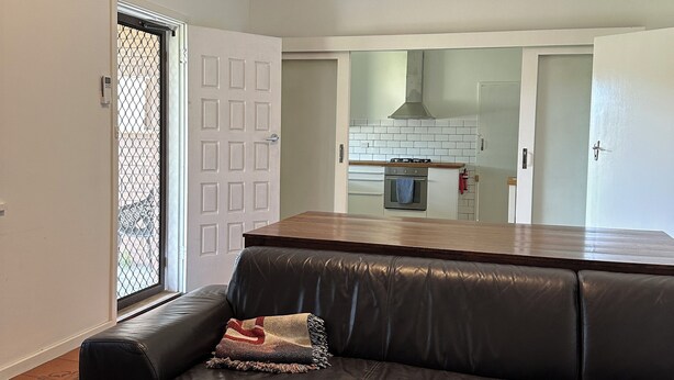 A modern living room with a black leather sofa, a wooden coffee table, and a view of the kitchen through an open door.
