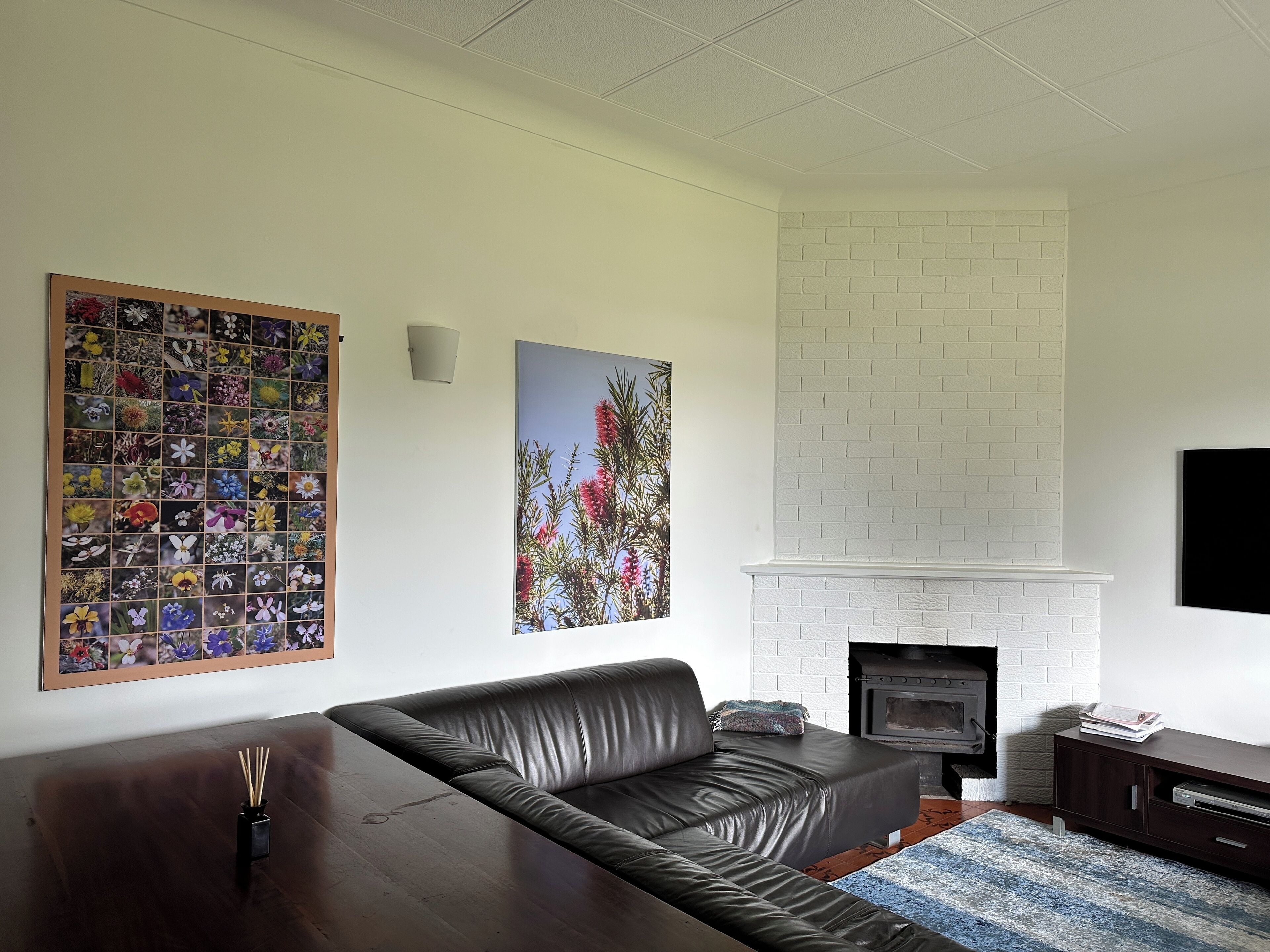 A living room with a black leather sofa, a fireplace, and a wall-mounted picture frame with multiple photos.