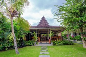 A covered pavilion with a tiled roof, surrounded by lush greenery and a stone pathway leading to it. - Puri Canggu Rooms 2 (Bali)