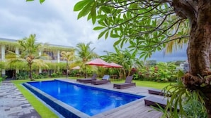 Une piscine entourée de plantes tropicales et dotée d’une terrasse en bois, avec des chaises longues et des parasols.