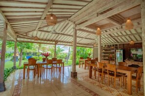 Un espace de restauration en plein air avec des tables et des chaises en bois, un sol carrelé et des luminaires suspendus.