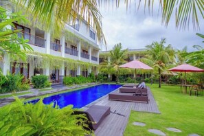 A pool area with lounge chairs, umbrellas, and a building with balconies. - Puri Canggu Rooms 2 (Bali)
