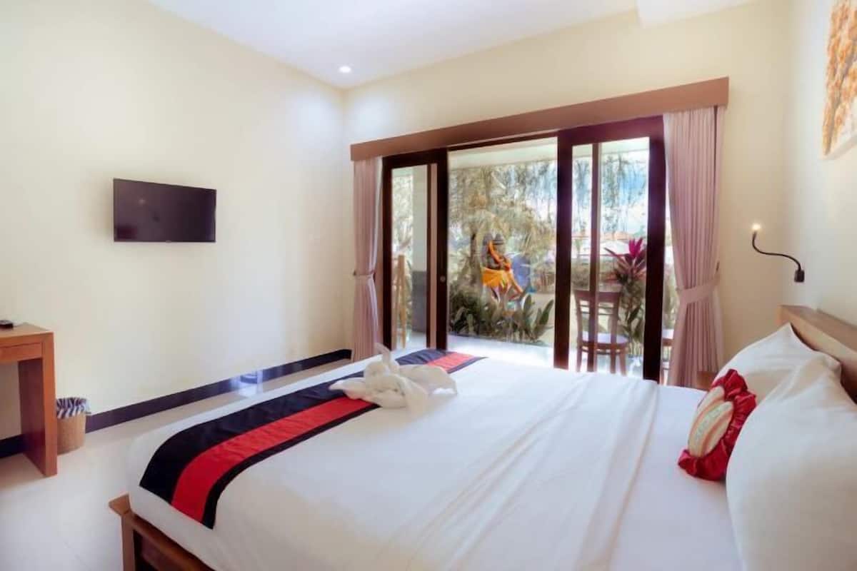A hotel room with a bed, a TV mounted on the wall, and a sliding glass door leading to an outdoor area.