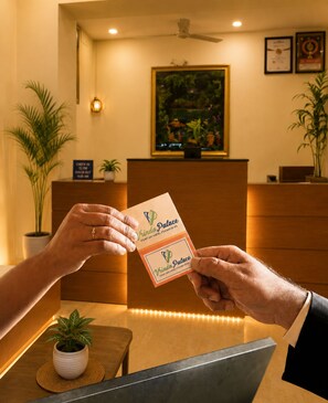 A reception desk with a framed picture, a ceiling fan, and a sign indicating check-in and check-out times. - Hotel vrinda palace  (Jaisalmer)