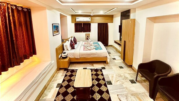Habitación de hotel con cama, mesita de noche, silla, armario y una pequeña mesa con alfombra.