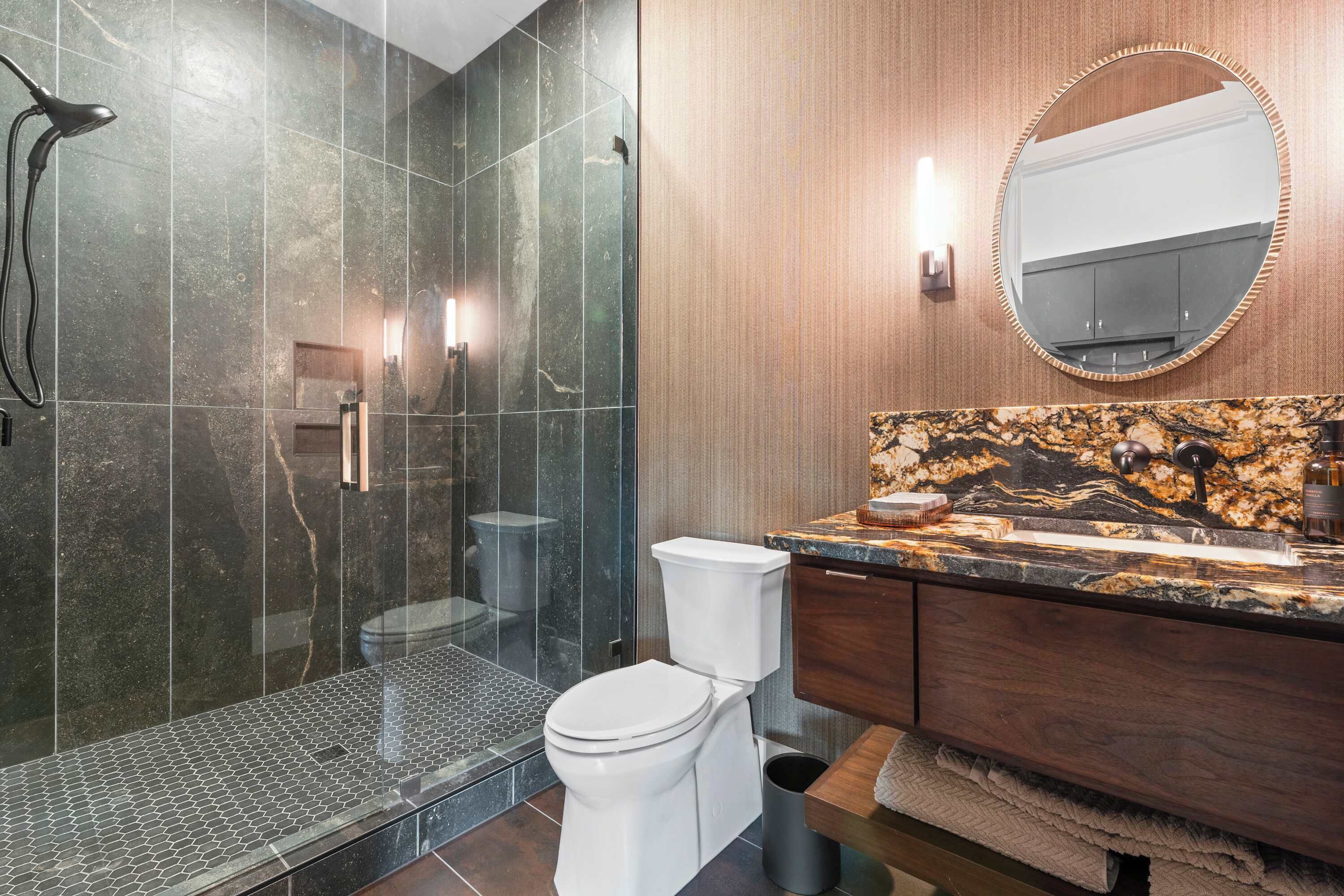 A modern bathroom with a glass-enclosed shower, a white toilet, and a marble vanity with a sink.
