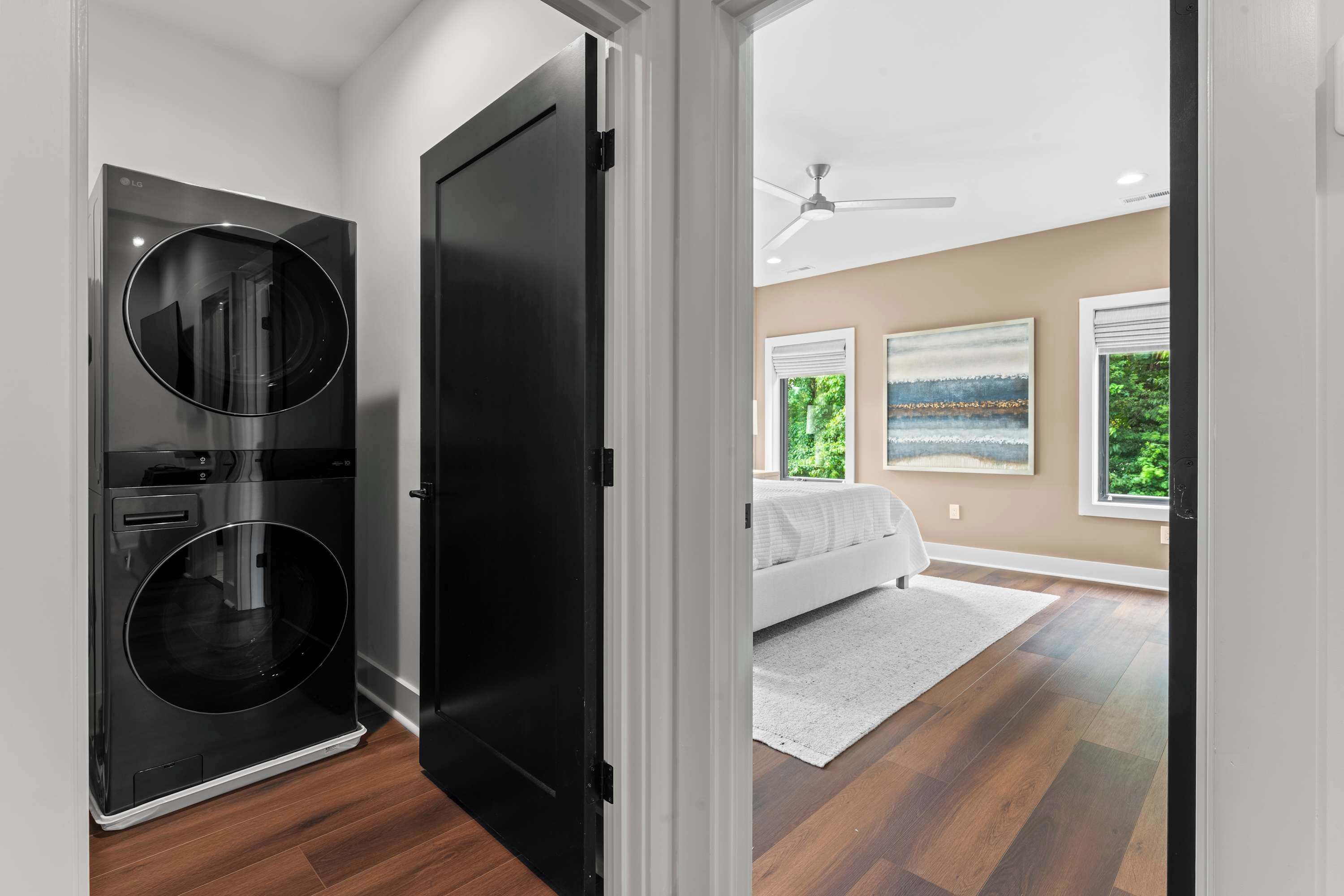 Un dormitorio moderno con una cama grande, un ventilador de techo y dos ventanas con vistas a follaje.