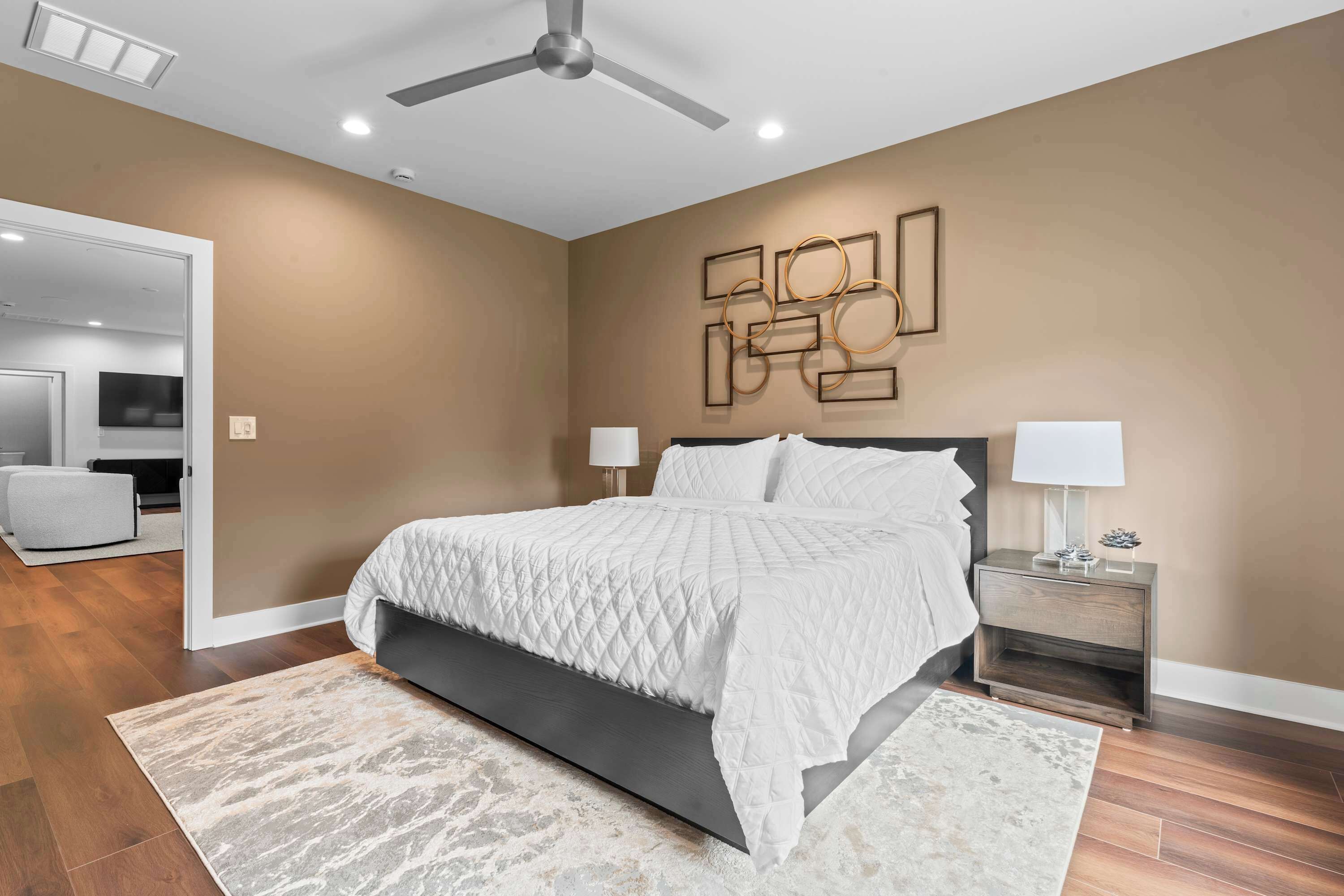 A modern bedroom with a bed, nightstands, a ceiling fan, and a wall art piece.