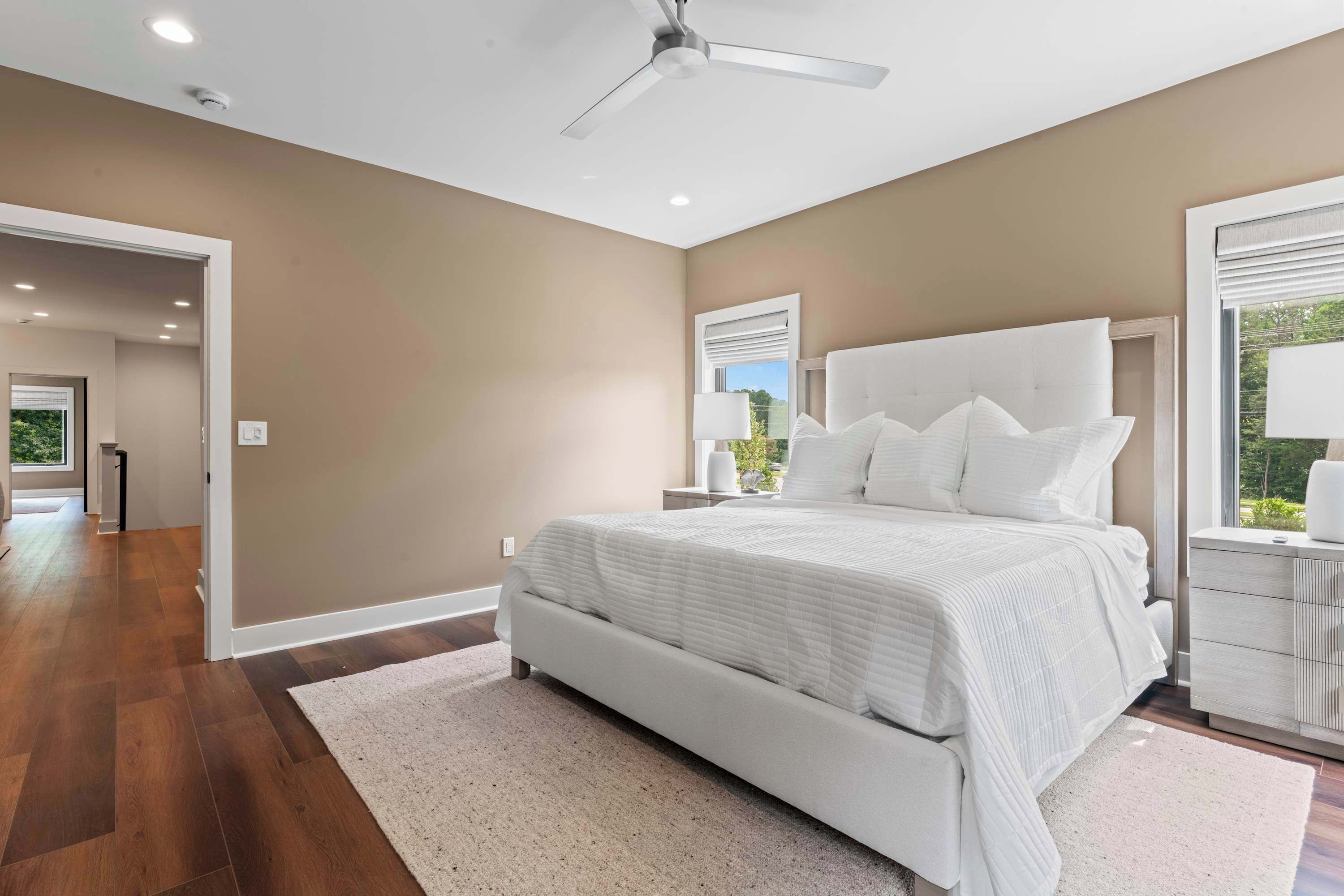 A bedroom with a large bed, a ceiling fan, and a view of the outdoors through a window.