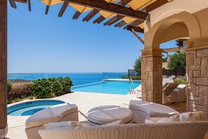 Un espace piscine avec vue sur la mer, des chaises longues et une pergola.