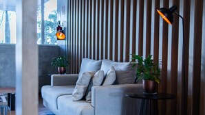 Un salon moderne avec un canapé gris, un mur lambrissé en bois et une petite table ronde surmontée d’une lampe.