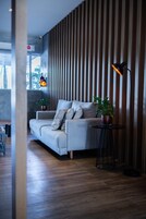 Una sala de estar moderna con un sofá gris, un muro de listones de madera y una pequeña mesa redonda con una lámpara.