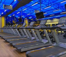 Varias caminadoras con pantallas digitales, bajo luces azules en un gimnasio.