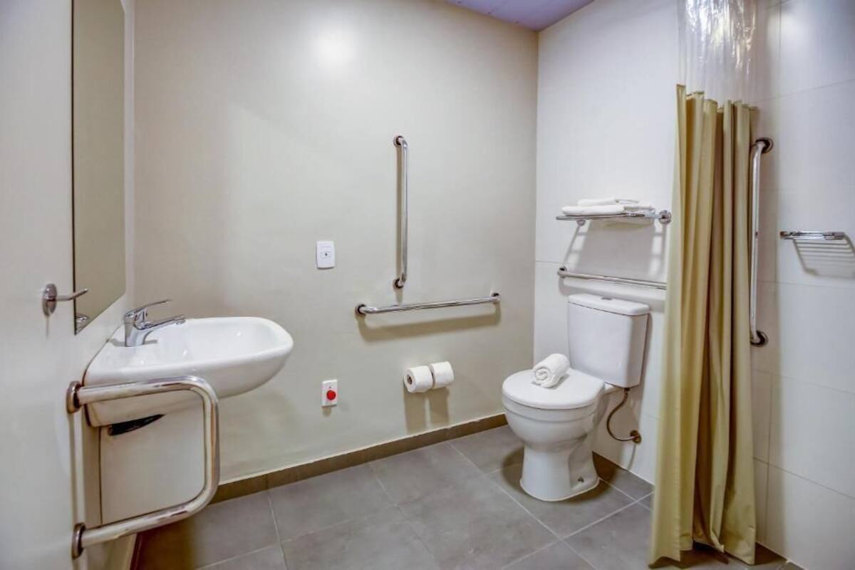 Un baño con lavamanos, inodoro y barras de apoyo.