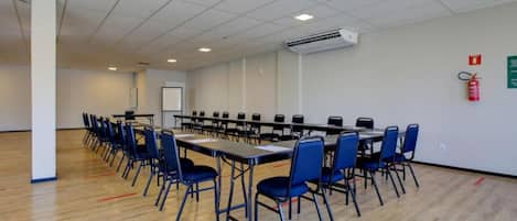Un salón de conferencias con una larga mesa, sillas azules y una unidad de aire acondicionado en el techo.