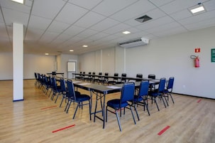 Uma sala de conferências com uma mesa comprida, cadeiras azuis e um aparelho de ar condicionado no teto.