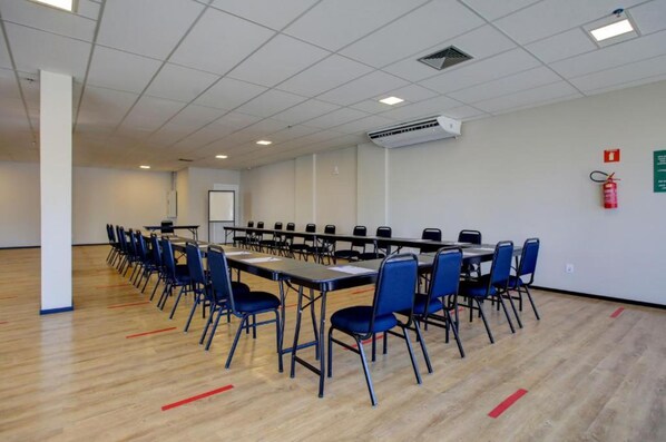 A conference room with a long table, blue chairs, and an air conditioning unit on the ceiling.