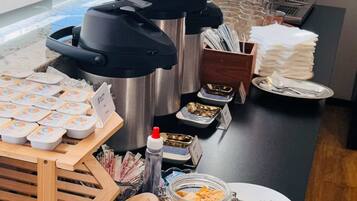 A buffet setup with various food items, a coffee machine, and condiments.