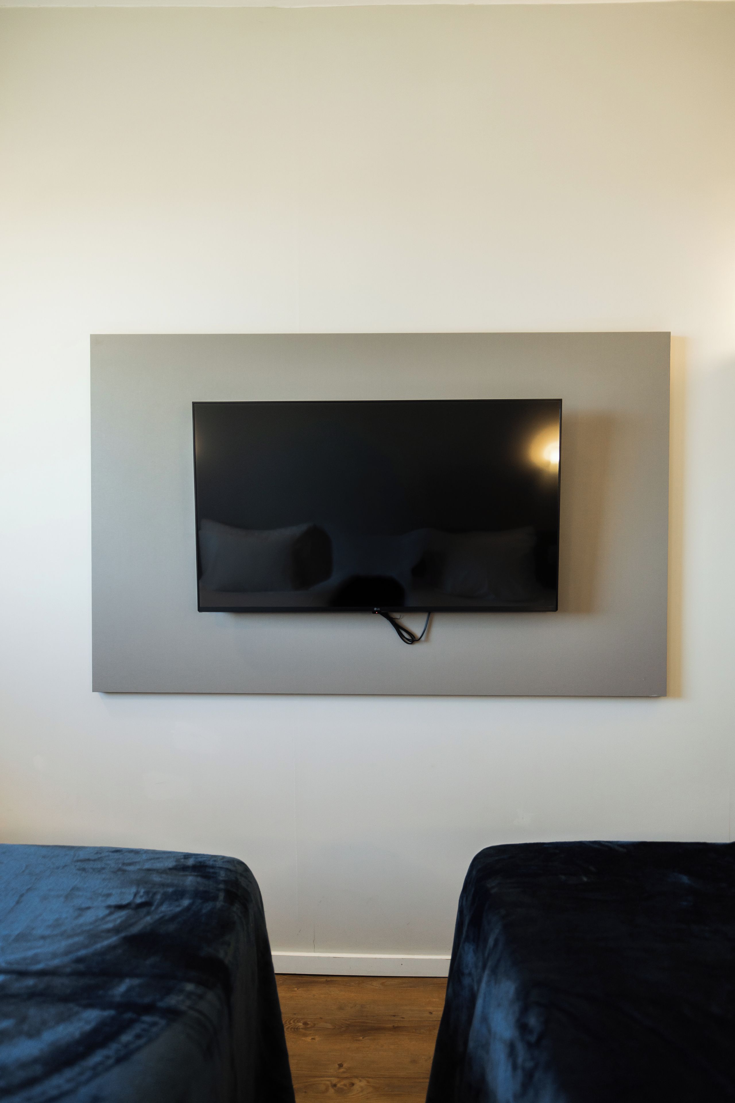 Una habitación con televisión montada en la pared y dos camas con cubrecamas oscuras.