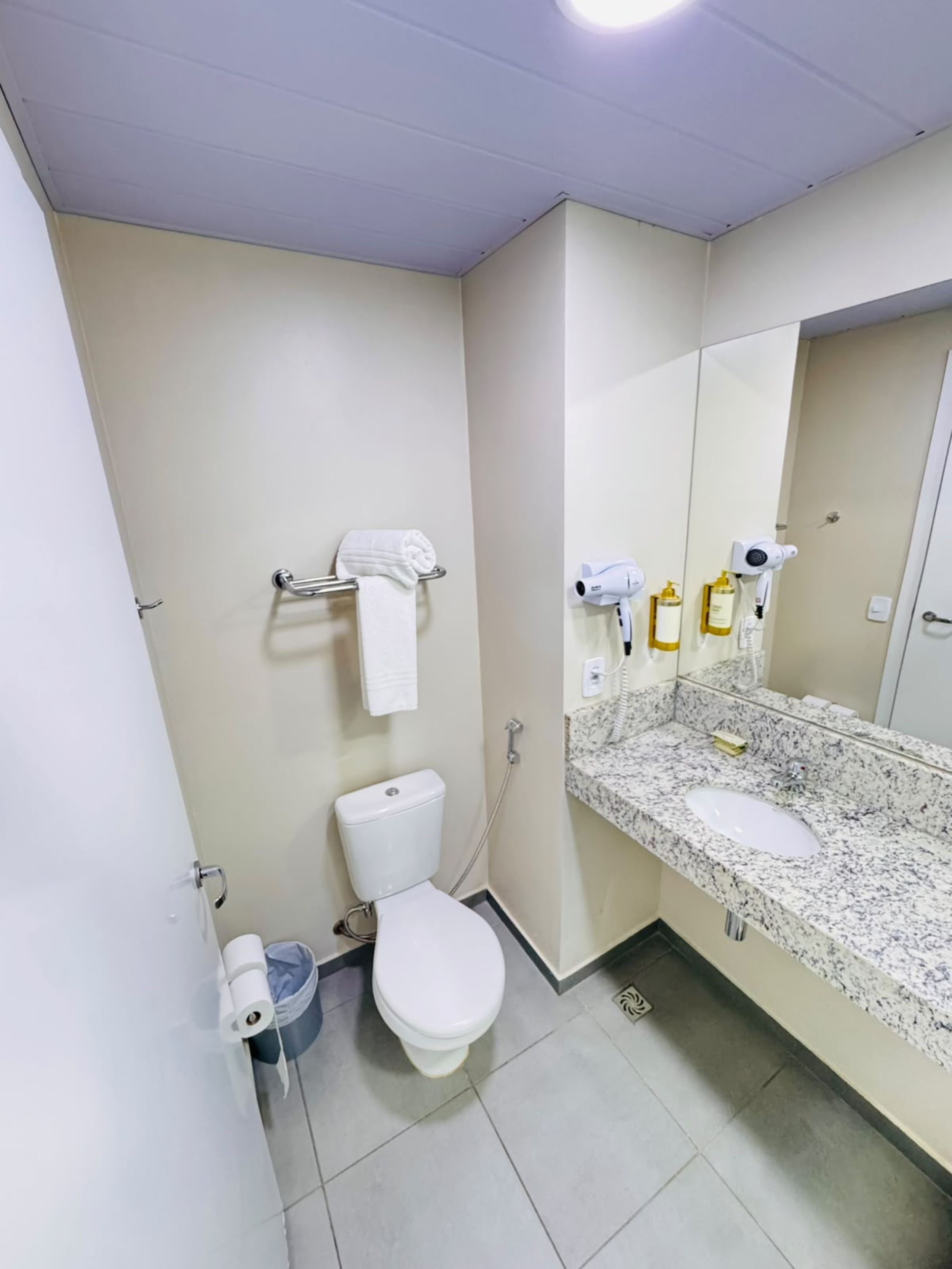 A bathroom with a toilet, sink, towel rack, and two hair dryers.