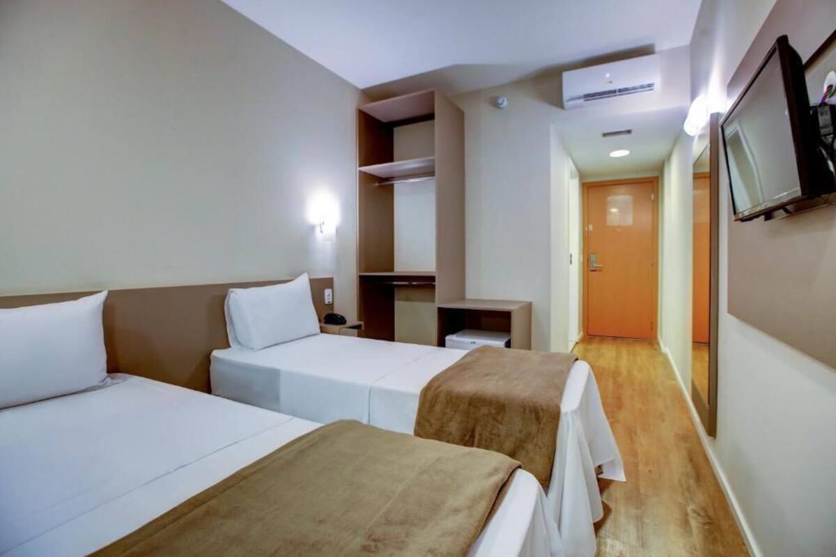 Habitación de hotel con dos camas, un escritorio pequeño, un televisor montado en la pared y suelo de madera.
