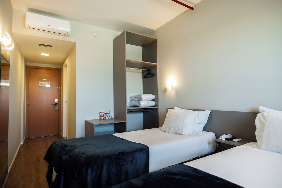A hotel room with two beds, a wardrobe, a small desk, and a hanging coat rack.