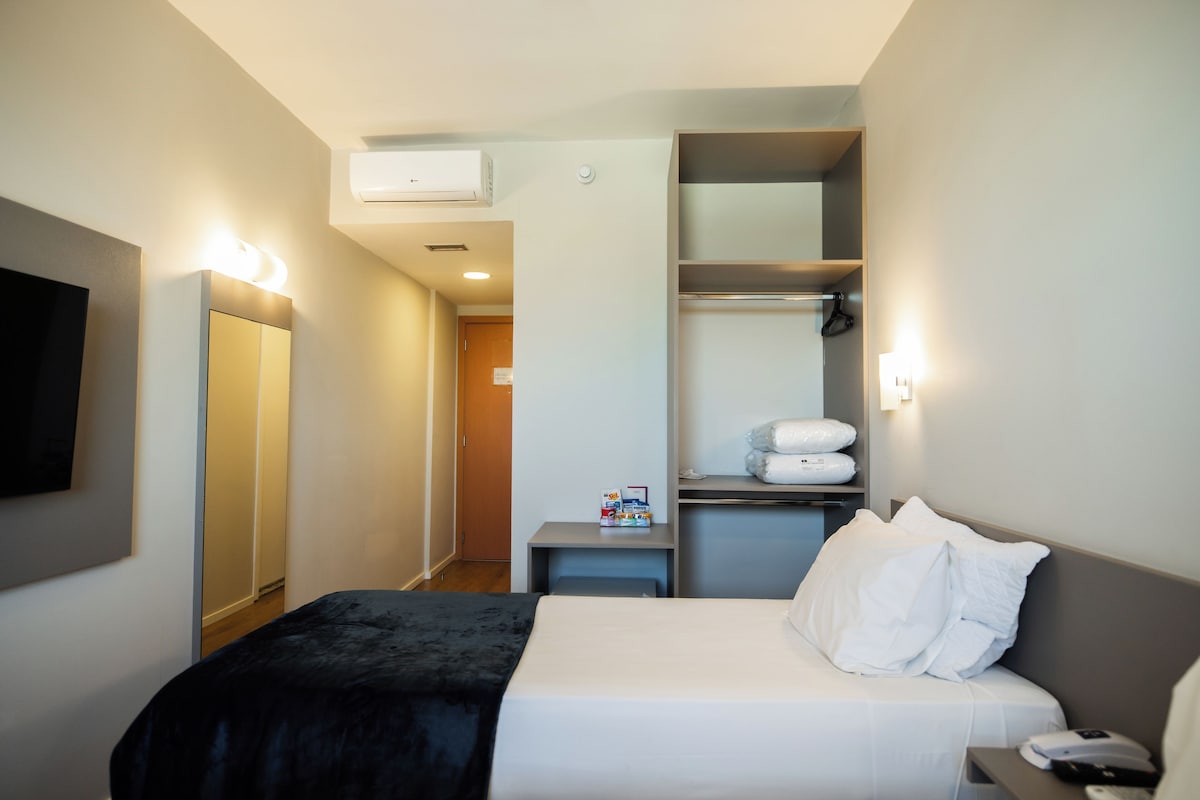 A hotel room with a bed, bedside table, and a wardrobe.