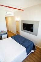 Habitación de hotel con cama, televisor montado en la pared, escritorio pequeño y un tubo rojo en el techo.