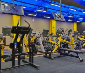 A gym with multiple exercise machines, including treadmills and weight machines, arranged in rows.