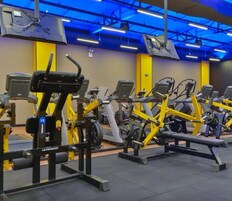 Uma academia com diversos equipamentos de exercícios, incluindo esteiras e aparelhos de musculação, dispostos em fileiras.