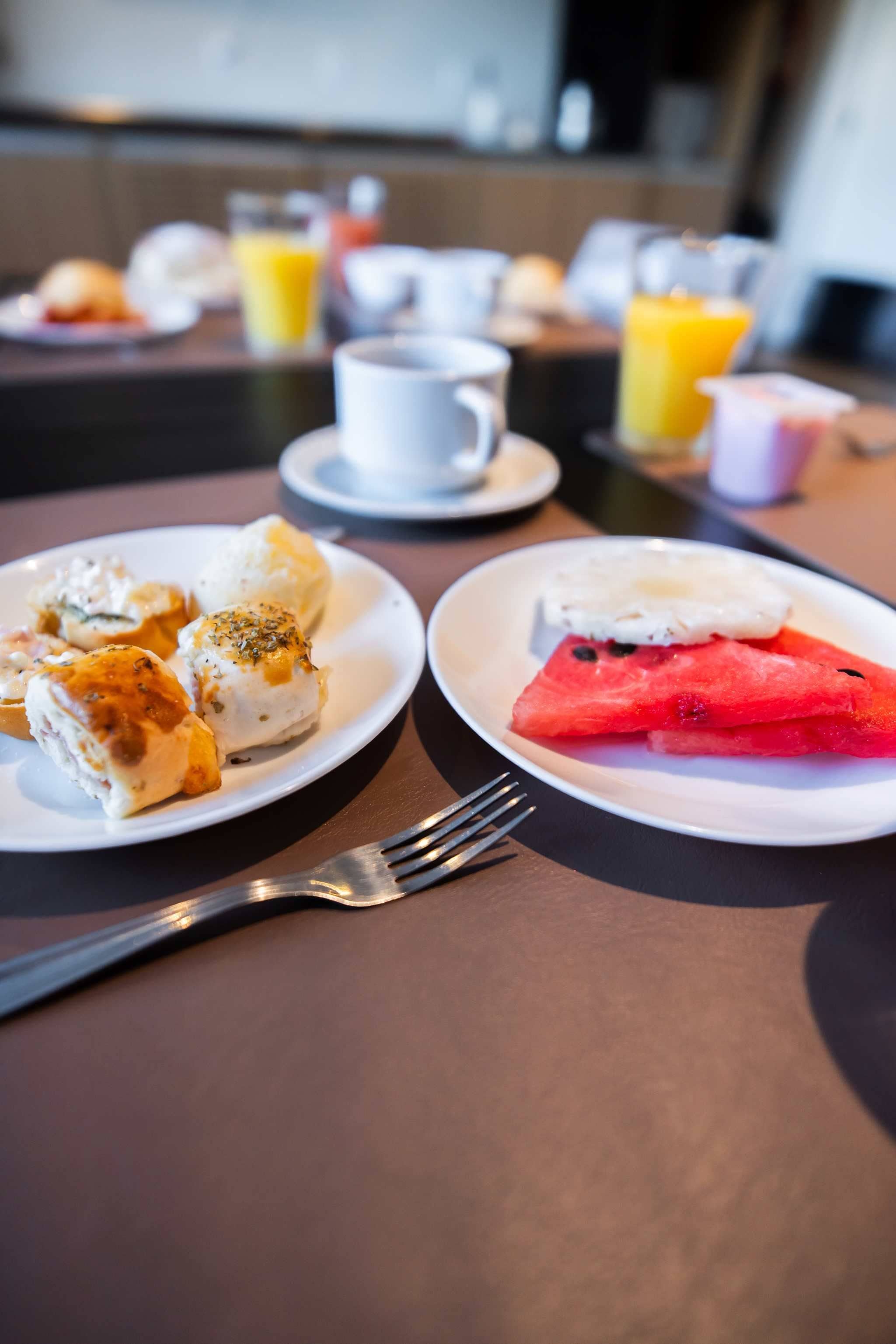 Mesa posta para o café da manhã, com pratos de comida, uma xícara e um garfo.