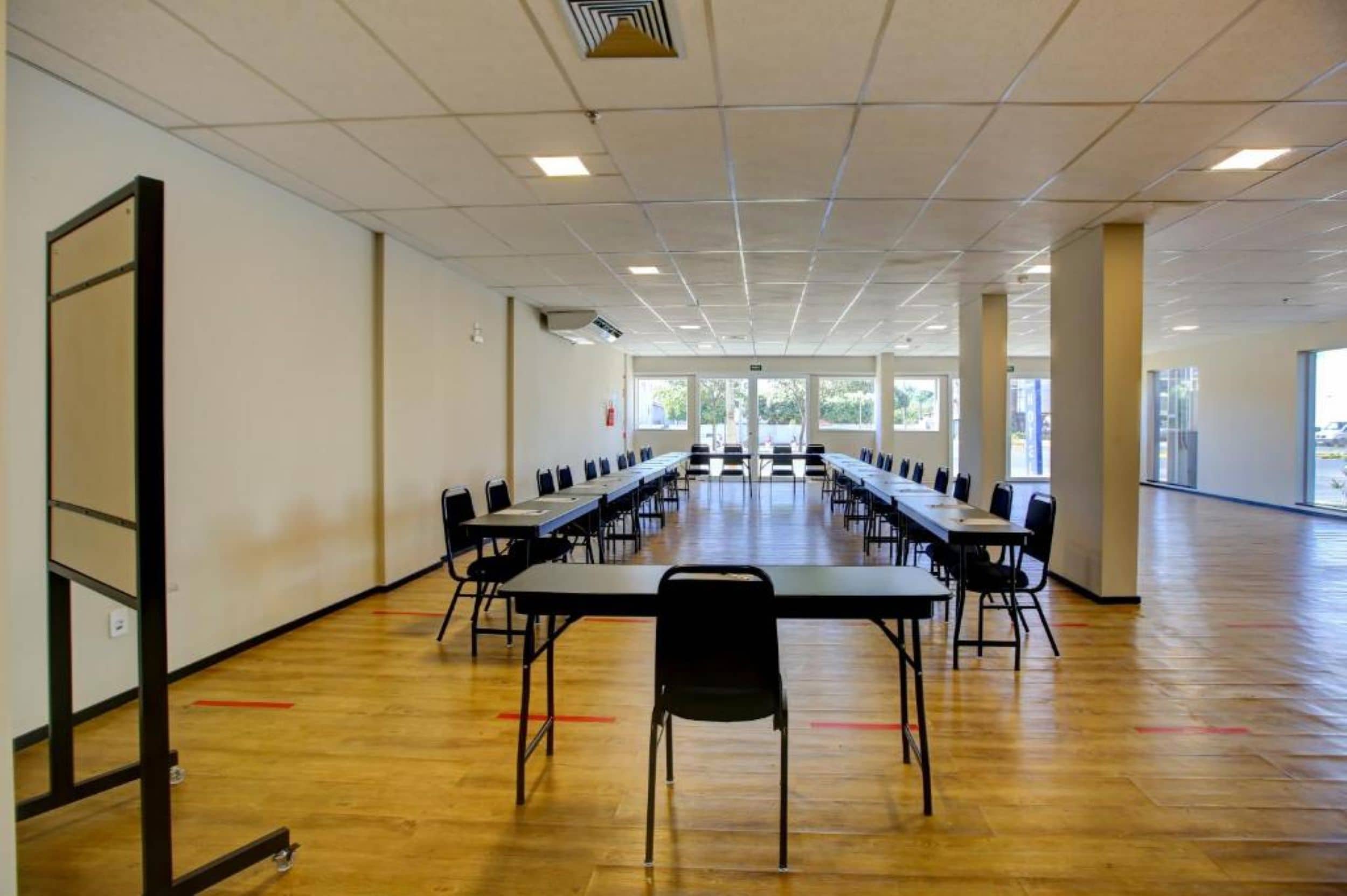 A conference room with long tables and chairs, large windows, and a wooden floor.