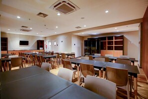 A conference room with multiple tables and chairs, a flat-screen TV mounted on the wall, and a wooden panel wall.