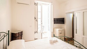 A bedroom with a bed, a wardrobe, a bedside table, a TV, and an open door leading to a balcony. - Palazzo Celina (Gallipoli)