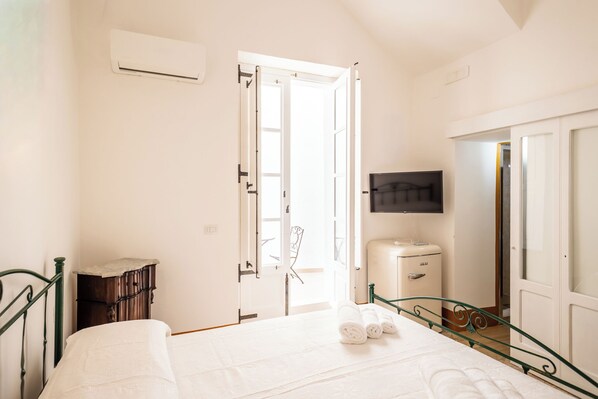 A bedroom with a bed, a wardrobe, a bedside table, a TV, and an open door leading to a balcony. - Palazzo Celina (Gallipoli)