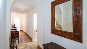 A hallway with a stone floor, an arched doorway, a wooden chair, and a large mirror with an ornate frame. - Palazzo Celina (Gallipoli)