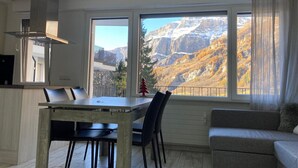 A modern kitchen with a dining area and a sofa, overlooking a mountainous landscape. - New Studio | Dream Views • Balcony • Free Parking (Leukerbad)