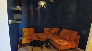 Un salon comprenant un canapé d’angle, une petite table ronde et une étagère fixée au mur.