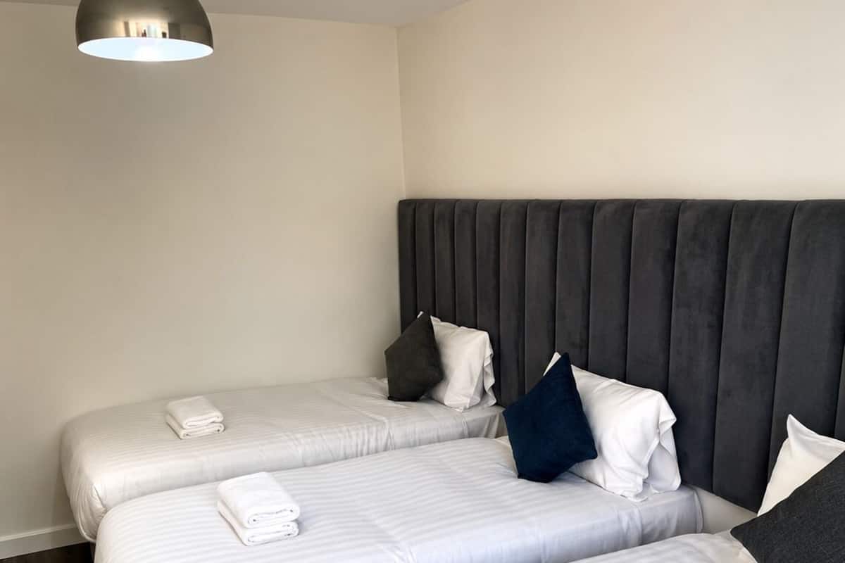 A hotel room with three beds, a dark headboard, and a hanging light fixture.