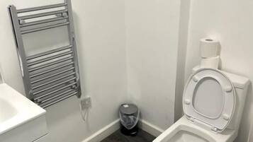 Un baño con inodoro blanco, toallero de metal, lavabo blanco y un cubo de basura.